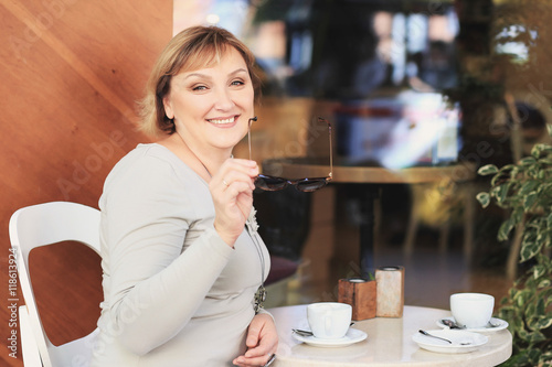 Beautiful woman is drinking coffee in the cafe. She has got blonde hair, green eyes, white skin. Smiling woman