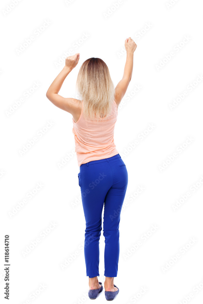 back view of dancing young beautiful woman. girl watching. Rear view people  collection. backside view of person. Isolated over white background. Blonde  in blue pants waving his hands to the music Stock