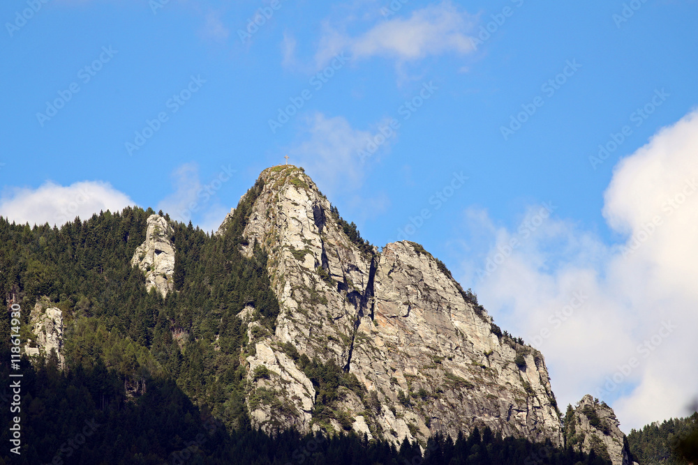 Mount Sassariente,Ticino, with its iron cross at the top against blue skies and white clouds