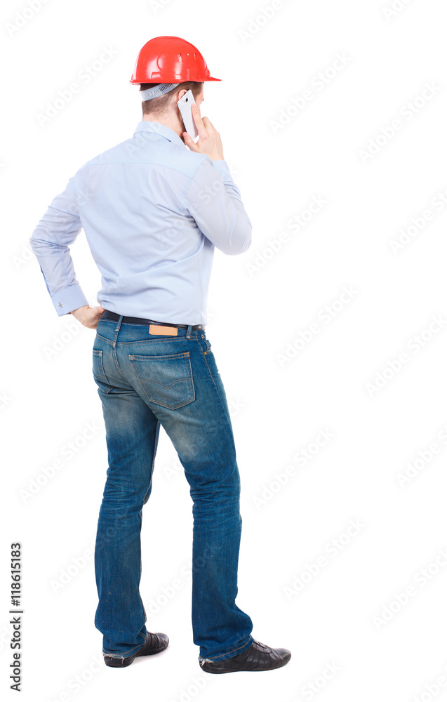 Backview of business man in construction helmet stands and enjoys tablet or using a mobile phone. Standing young guy. Rear view people collection. backside view of person. Isolated over white Backview of business man in construction helmet stands and enjoys tablet or using a mobile phone. Standing young guy. Rear view people collection. backside view of person. Isolated over white