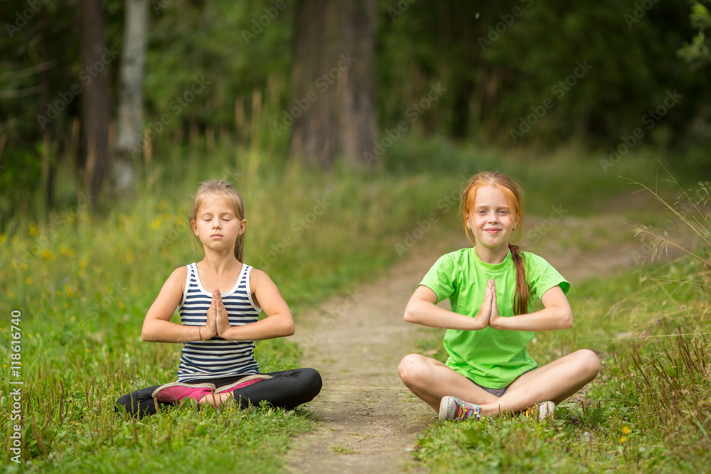 Fototapeta premium Two fun little girls sitting in yoga meditation outdoors.