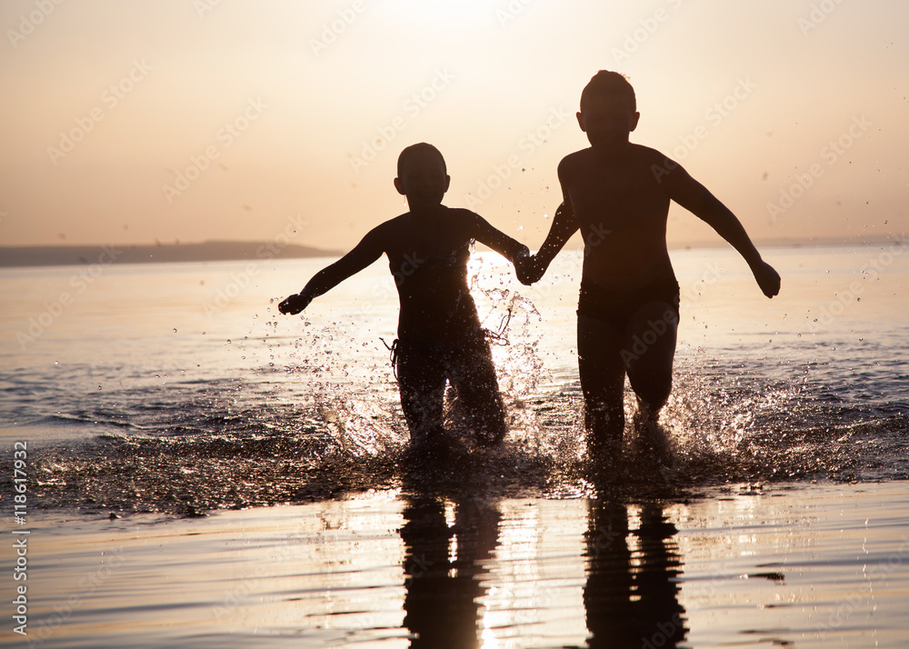 Fototapeta premium Children run along the water at sunset