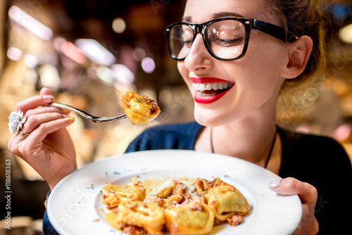 Young woman eating tortellini pasta in front of the food shop in Bologna. Tortellini ring-shaped pasta was invented in Bologna.
