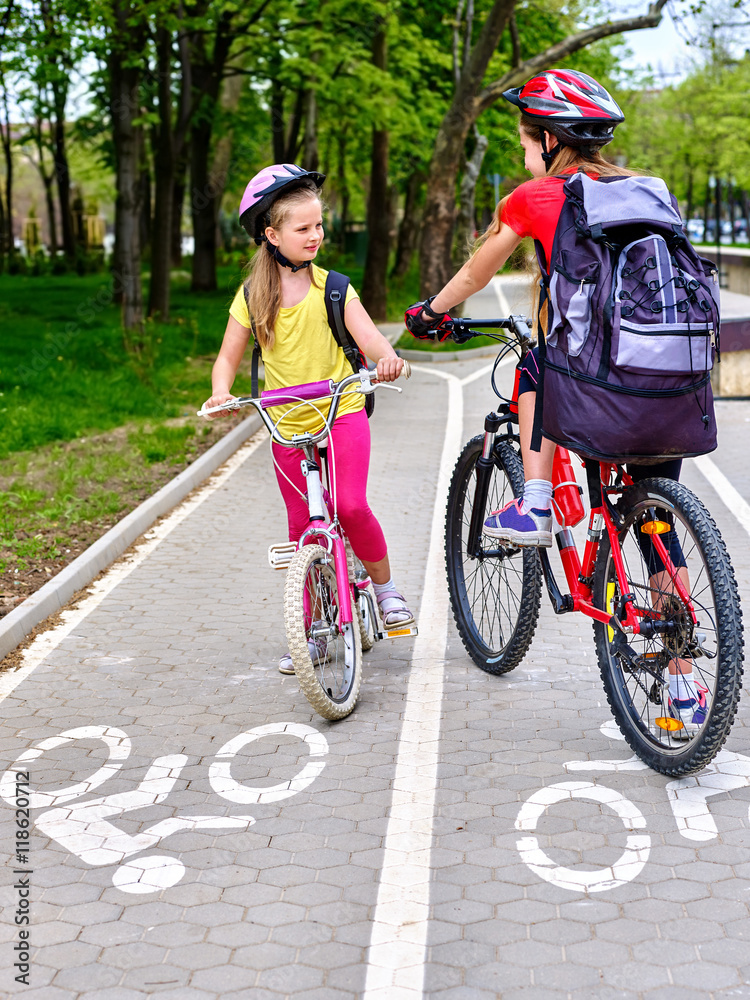 Obraz premium Bicycle girls wearing bicycle helmet and glass with rucksack ride on bicycle. Girls children cycling meet on white bike lane. Bike share program save money and time at city street.