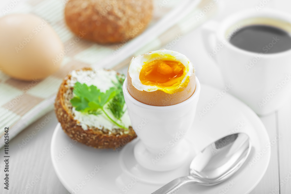 Perfect soft boiled egg, open bread sandwich with butter and cup of coffee on a table. Traditional food for healthy breakfast.