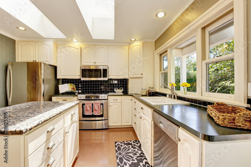 White kitchen with granite tops. Kitchen island and tile floor.