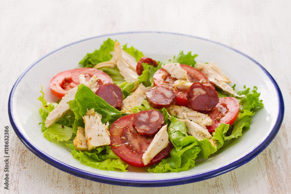 fresh salad with chicken and chourico on white dish on white wooden background