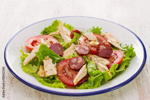 fresh salad with chicken and chourico on white dish on white wooden background