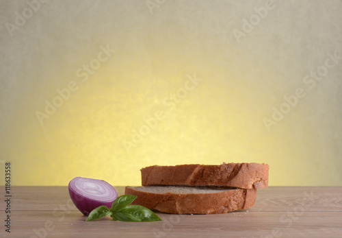 Rye bread, basil and red bulb onion on a wooden table at sunrise.
