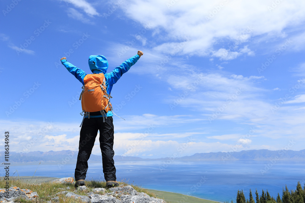 cheering woman hiker open arms on mountain peak