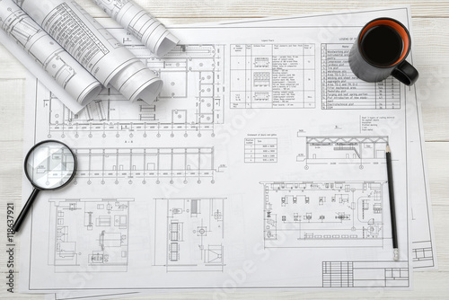 Top view of draftsman's workplace with plan, magnifier, pencil, mug coffee and rolled drafts