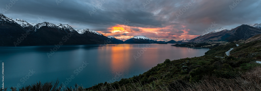 Panoramic view along the road from Queenstown to Glenorchy overlooking Lake Wakitipu and surrounding snow-capped mountains at sunset, New Zealand.