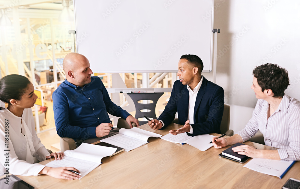 Fototapeta premium Business meeting between 4 unique individuals, both male and female, with a mixed race businessman busy speaking to the other educated individuals.