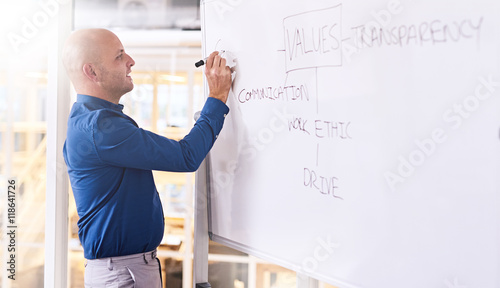 Young caucasian male busy writing on a white board during his presentation about the values he feels people should aspire to. and he encourages in his own firm.