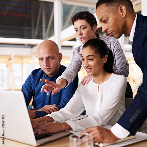 Square image of a diverse group of business individuals busy looking at the latest stock market trends on a laptop screen to see if the can spot patterns together.