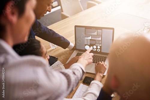 Group of four people pointing to and analysing graphs and charts all displayed on a notebook in front of them to determine performance goals for the next year as a group. photo