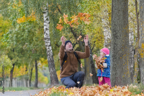 Father with raised hands tossing up yellow fallen leaves with his daughter in colorful autumn park outdoors © nkarol
