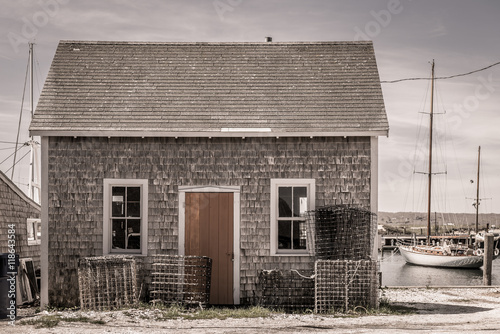 Old rundown fishing shack with lobster traps and boats in the background in a quaint New England coastal village.