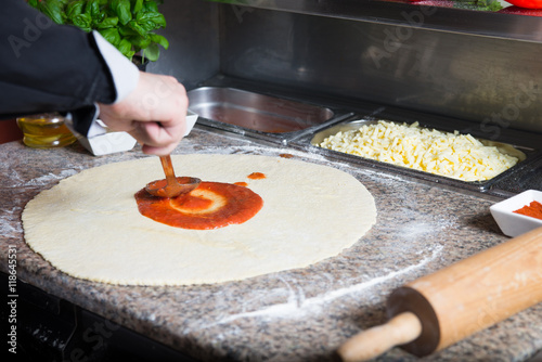 Chef smear pizza dough with tomato sauce. photo