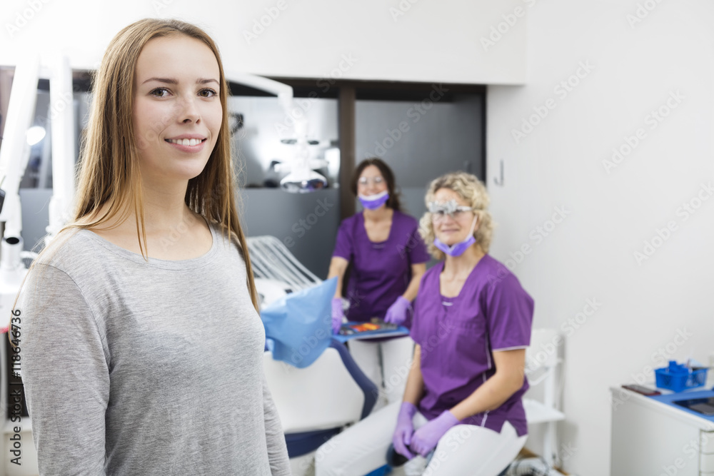 Smiling Female Patient With Dentists Working In Background Smiling Female Patient With Dentists Working In Background