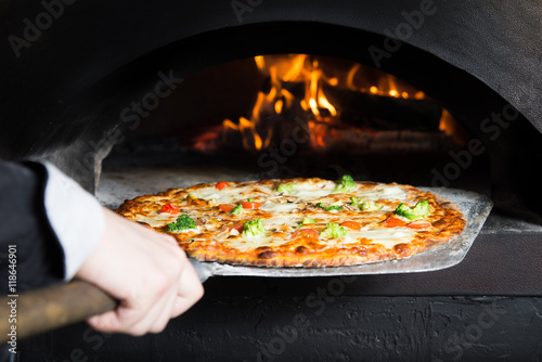 Hot pizza is removing from hot slove where it was baked. Cook using special shovel to removing them. This restaurant have special wood-fired oven. 