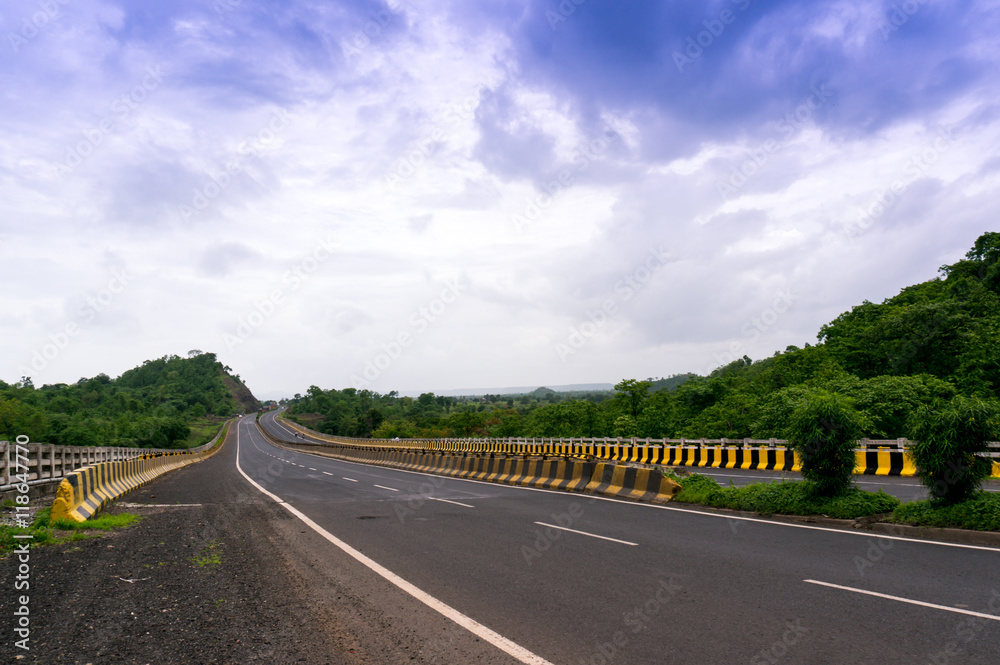 Empty road borded by  hills with cloudy skies 