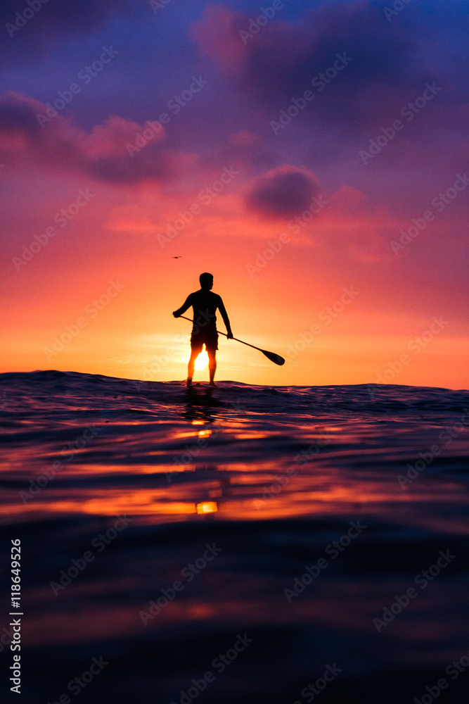 Surfer standing on his paddle board looking the sunset