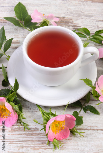 Cup of tea and wild rose flower on old rustic wooden background