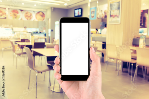 hand holding the phone tablet on blur restaurant background ; vintage tone style