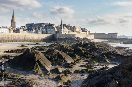 A view of the old walled city of Saint Malo in Brittany, France, from the sea bottom at low tide with huge stone blocks on the uncovered sea floor.