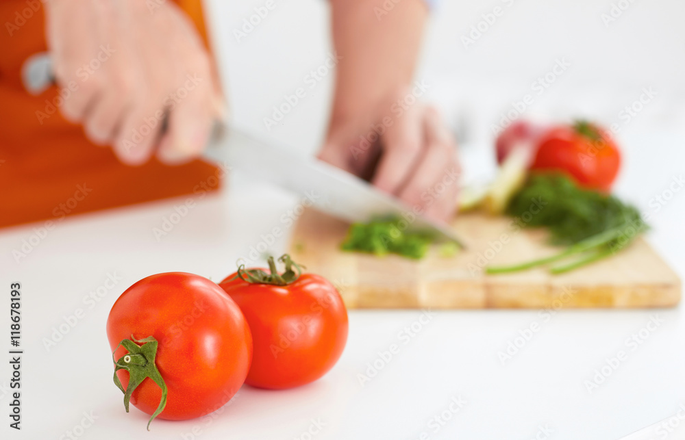 Two ripe tomatoes in the foreground . Man is cutting ripe vegetables on a wooden board in the background. Two ripe tomatoes in the foreground . Man is cutting ripe vegetables on a wooden board in the background.