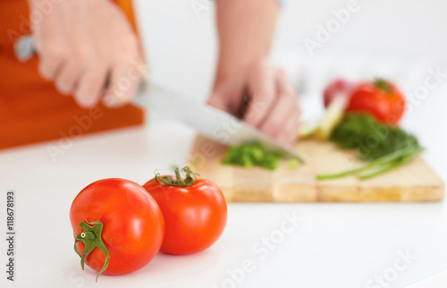 Two ripe tomatoes in the foreground . Man is cutting ripe vegetables on a wooden board in the background.
