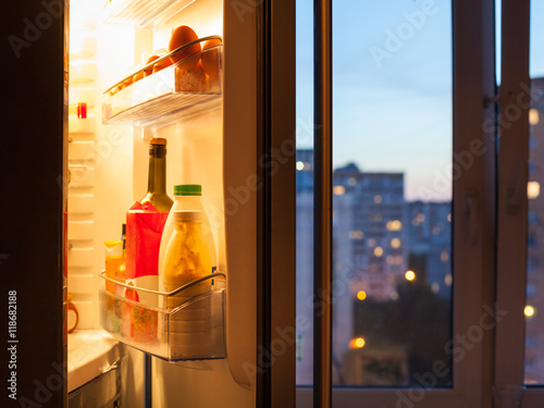 Open door of refrigerator with food in evening