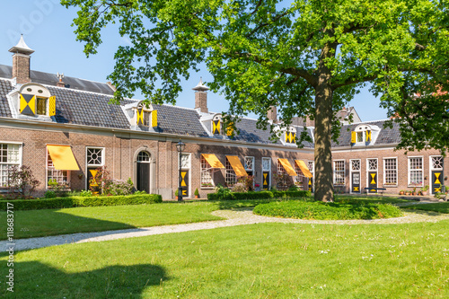 Fototapeta Green courtyard surrounded by old almshouses in Hofje van Staats in city of Haar