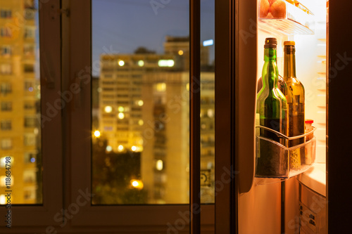 Open refrigerator with wine bottles in night