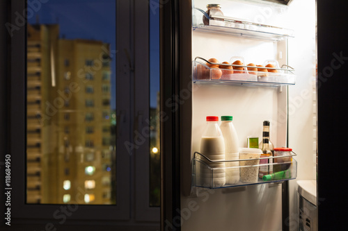 door of home fridge with dairy products in night