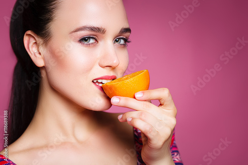 Portrait of comic happy girl holding halves of orange near face,