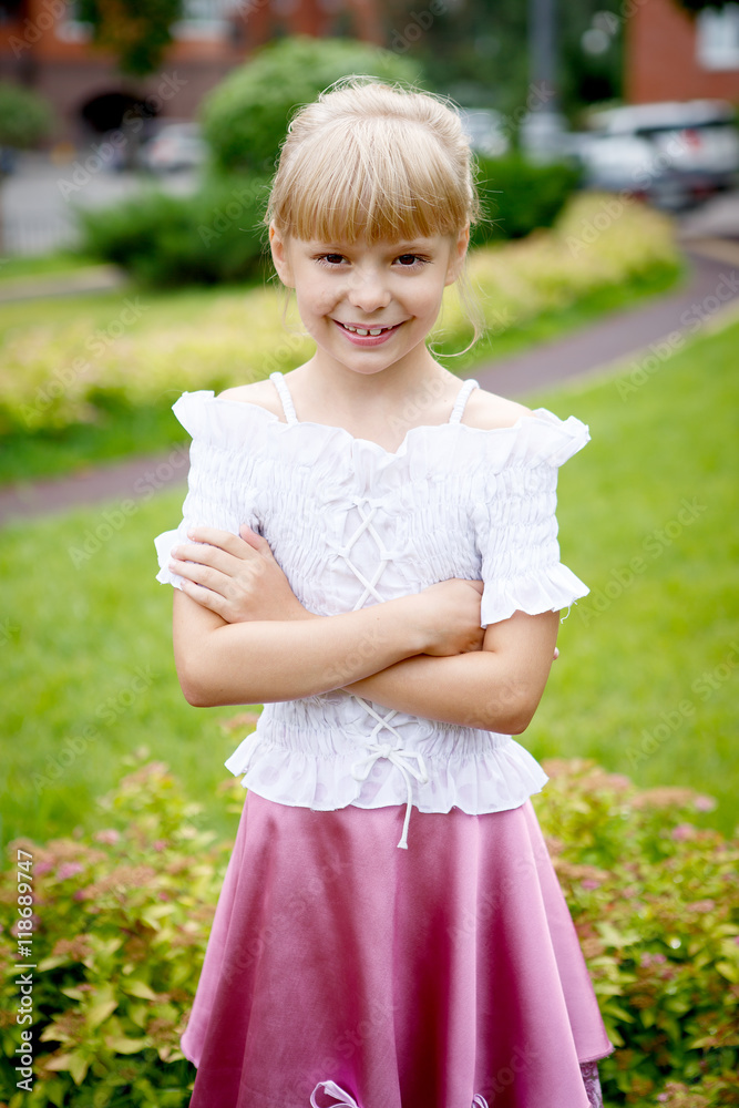 Portrait of beautiful little girl in a white blouse with a pink skirt in the Park