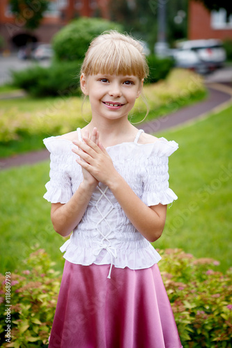 Portrait of beautiful little girl in a white blouse with a pink skirt in the Park