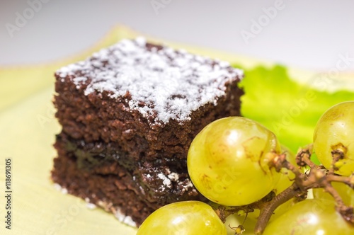 Chocolate sponge cake with icing sugar and grapes on the yellow tablecloth