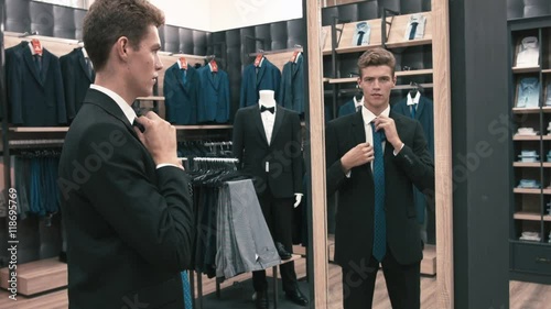 The man in the fitting room, looking in the mirror corrects tie in shop