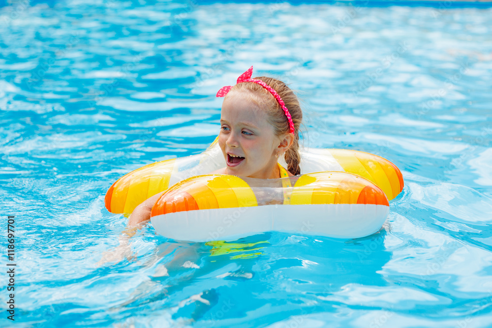 Cute little girl swimming in the pool in rubber ring, having fun in aquapark, happy summer holidays on the beach