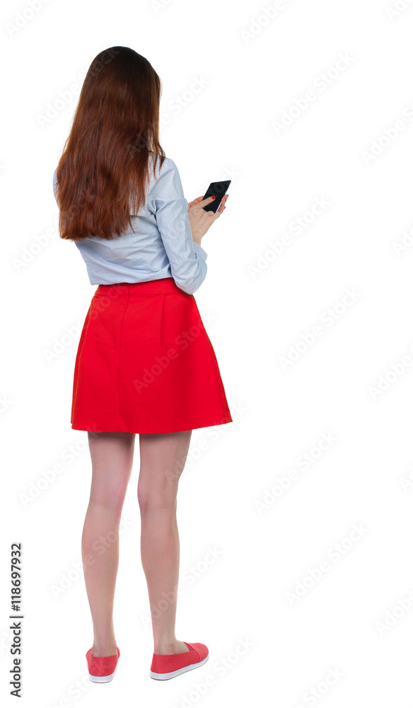 back view of standing young beautiful woman using a mobile phone or tablet computer. girl watching. Rear view people collection. backside view of person. Isolated over white background. Long back view of standing young beautiful woman using a mobile phone or tablet computer. girl watching. Rear view people collection. backside view of person. Isolated over white background. Long