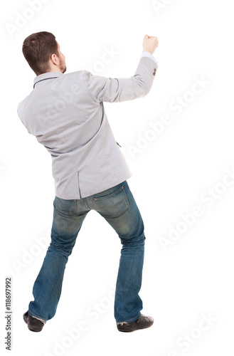 back view of standing man pulling a rope from the top or cling to something. Rear view people collection. backside view of person. Isolated over white background. A guy in a gray jacket, pulls a