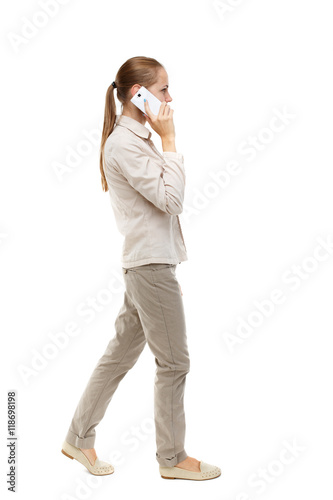 side view of a woman walking with a mobile phone. back view ofgirl in motion. backside view of person. Rear view people collection. Isolated over white background. Skinny girl in white denim suit