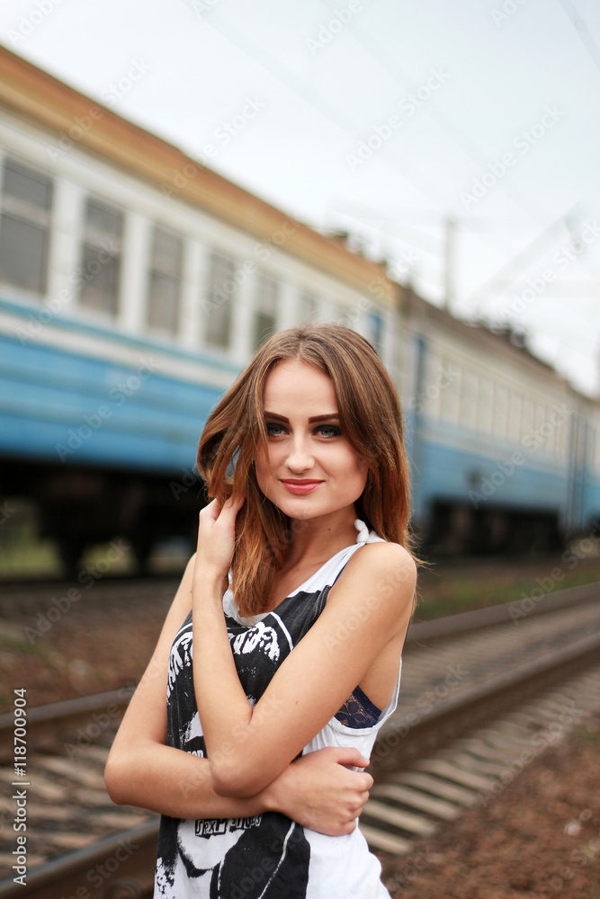 portrait of a young beautiful woman. Outdoor portrait of a young cute blond woman with a long hair and train background. Girl standing on railroad tracks.