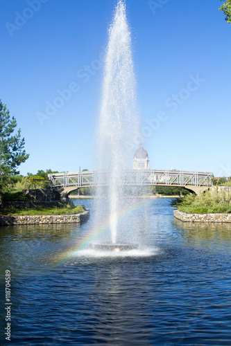 Early morning rainbow in a fountain in Wascana Park in Regina Saskatchewan. In the background is the Saskatchewan Legislature and a walking bridge.