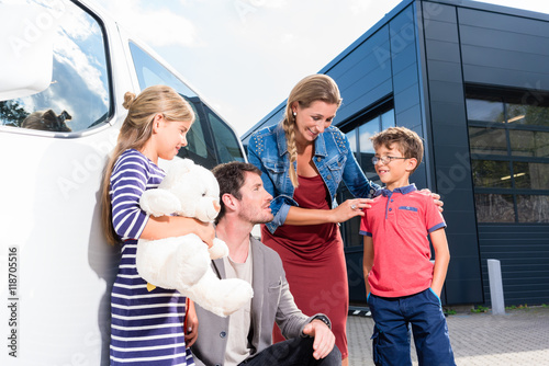 Familie mit Kindern kauft Auto im Autohaus und steht vor dem Neuwagen