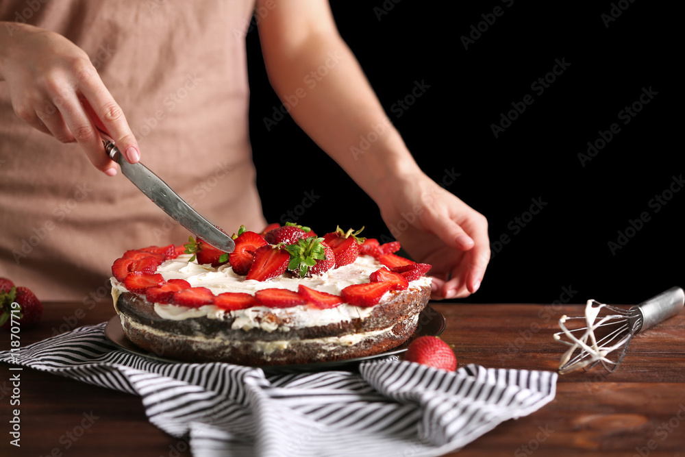 Woman slicing appetizing cake decorated with strawberry