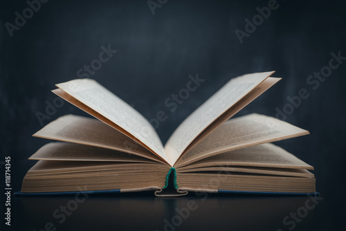 Раскрытая книга лежит на столе на фоне школьной доски черного цвета 
